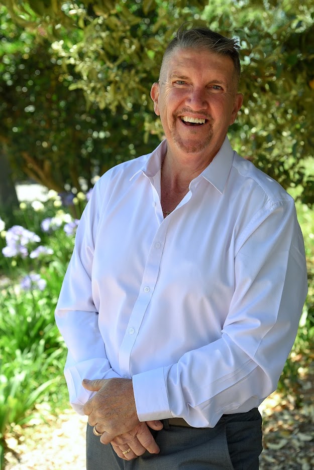 Mark smiling in a leafy outdoor setting